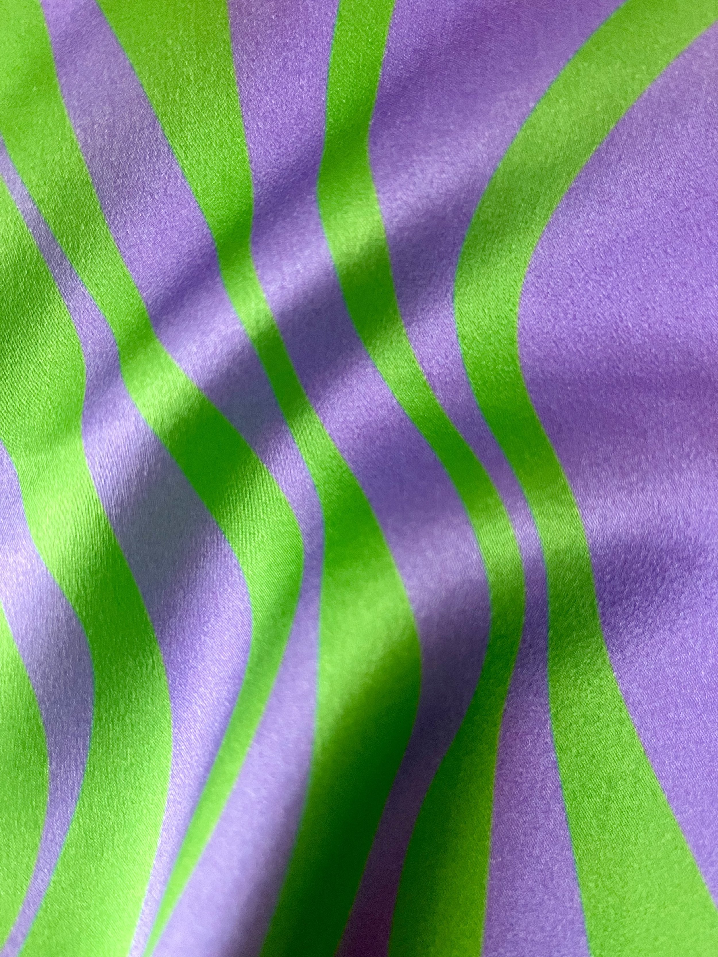 Close-up of lustrous bespoke silk satin textile design by Kika Pierides with vertical wavy stripes in vibrant green and purple